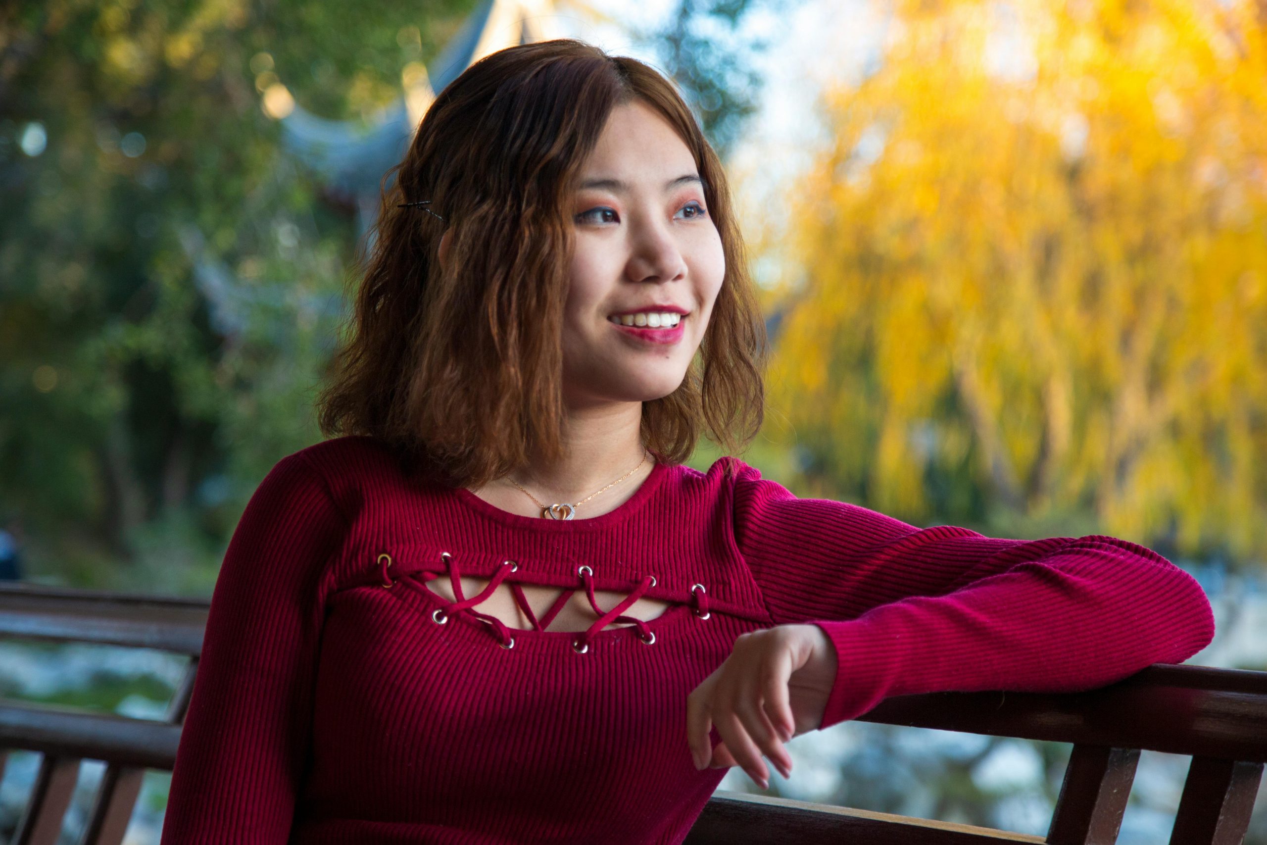 A smiling woman in a red sweater enjoys a fall day outdoors in Los Angeles park.