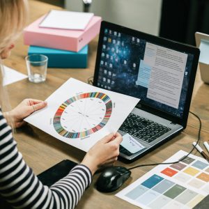 Businesswoman reviews color wheel and strategy documents on a laptop in an office setting.